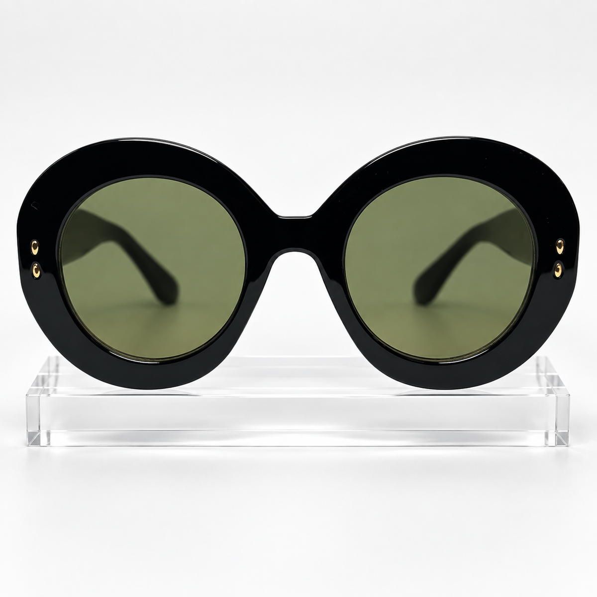 Oversized round sunglasses with a glossy black frame and olive green lenses, displayed on a clear acrylic stand against a white background.