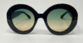 Oversized round sunglasses with a thick black frame and gradient lenses that fade from green at the top to beige at the bottom, shown against a plain white background.
