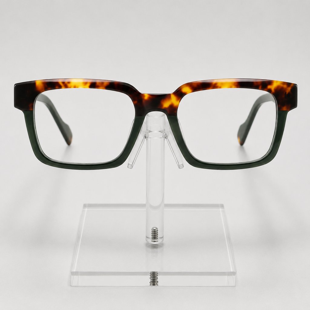 Rectangular eyeglasses with a dark green and amber tortoiseshell acetate frame, displayed on a clear acrylic stand against a light gray background.