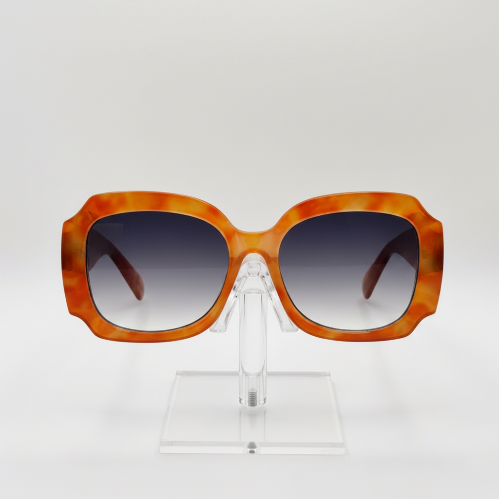 Oversized square sunglasses with a translucent orange and yellow marbled acetate frame and dark gradient lenses, displayed on a clear acrylic stand against a light gray background.