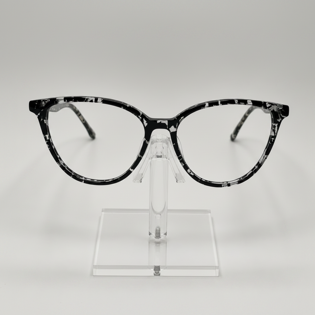 Black and white marbled cat-eye eyeglasses displayed on a clear acrylic stand against a light gray background.