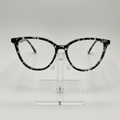 Black and white marbled cat-eye eyeglasses displayed on a clear acrylic stand against a light gray background.