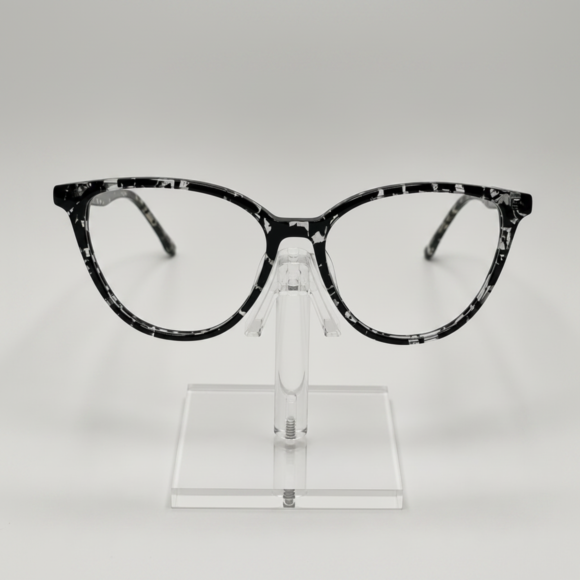 Black and white marbled cat-eye eyeglasses displayed on a clear acrylic stand against a light gray background.