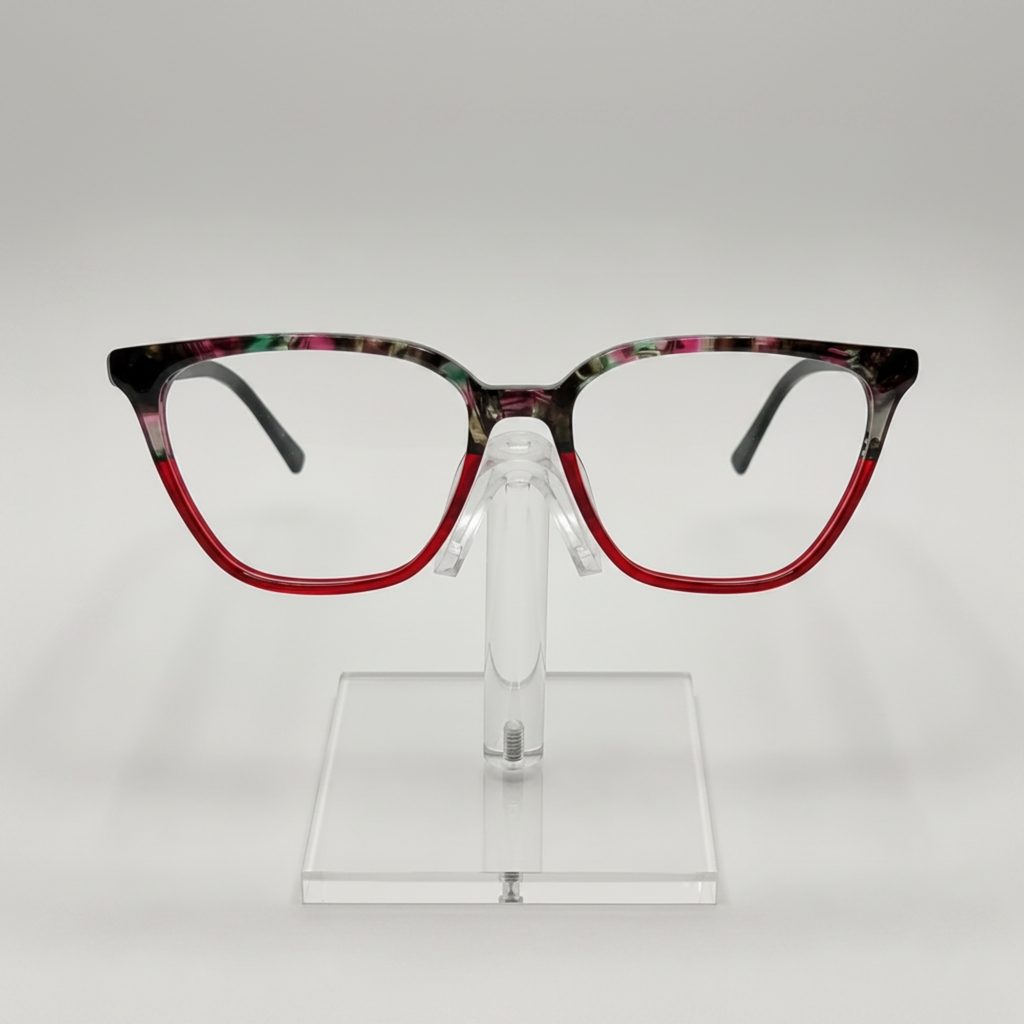 Fashionable square eyeglasses with a red acetate lower frame and a black, green, and pink marbled top frame, displayed on a clear stand against a light gray background.