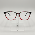 Fashionable square eyeglasses with a red acetate lower frame and a black, green, and pink marbled top frame, displayed on a clear stand against a light gray background.