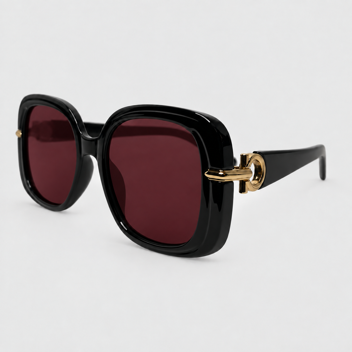 Black oversized square sunglasses with dark red lenses and gold-tone hardware on a light gray background.
