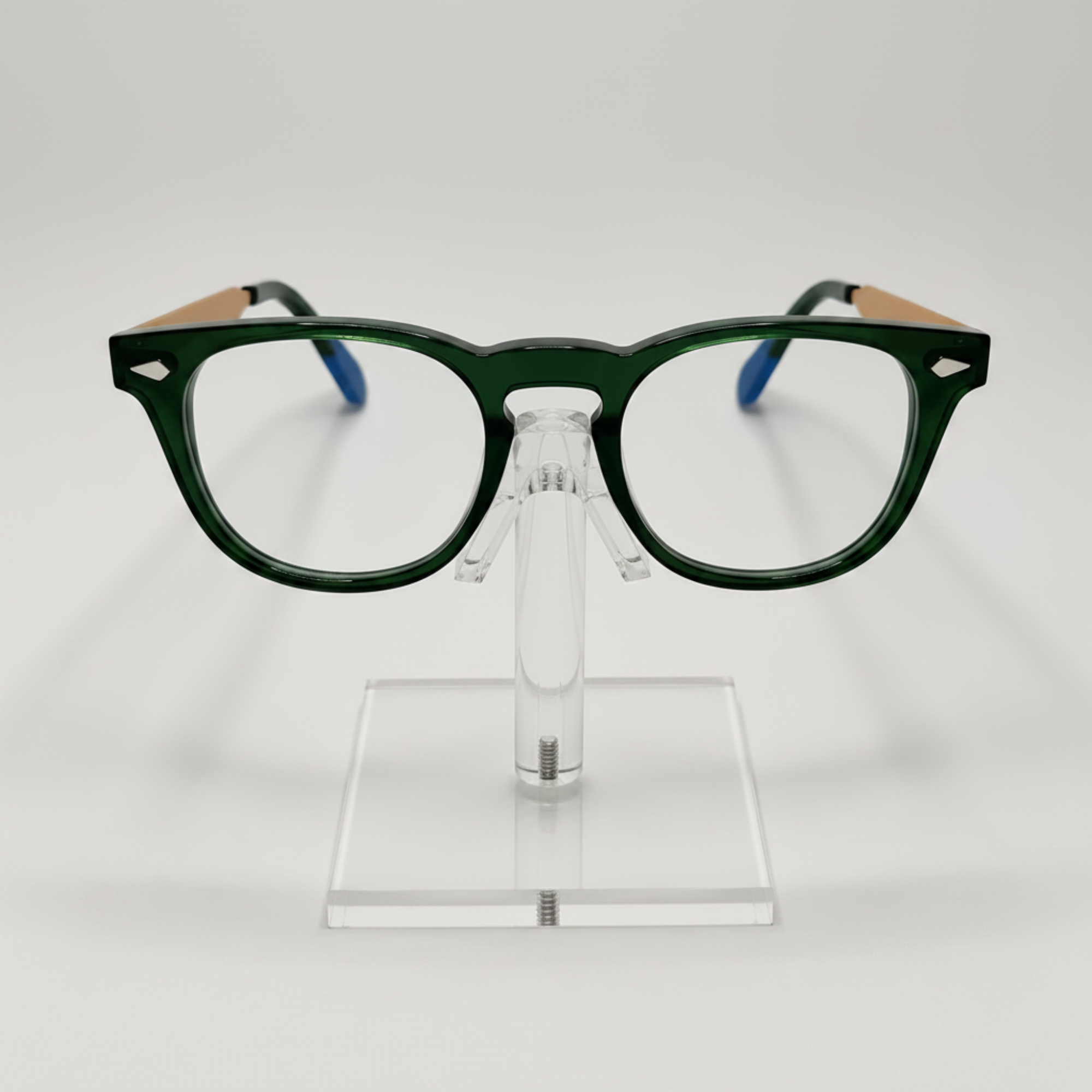 Dark green acetate eyeglass frames with light wood-look temples and blue temple tips, displayed on a clear acrylic stand against a light gray background.
