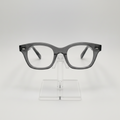 Gray acetate eyeglass frames with a thick, rounded rectangular shape, displayed on a clear acrylic stand against a light gray background.