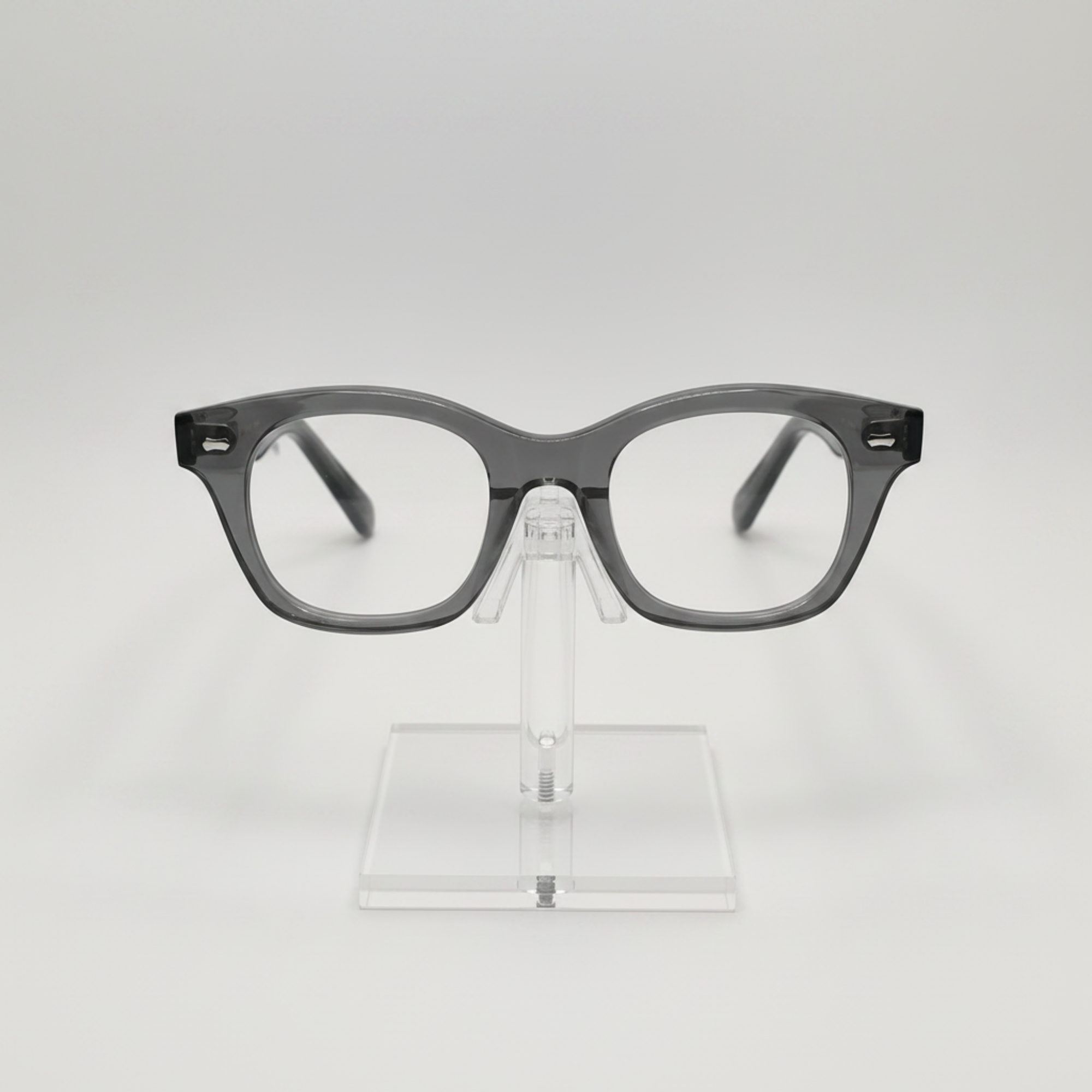 Gray acetate eyeglass frames with a thick, rounded rectangular shape, displayed on a clear acrylic stand against a light gray background.