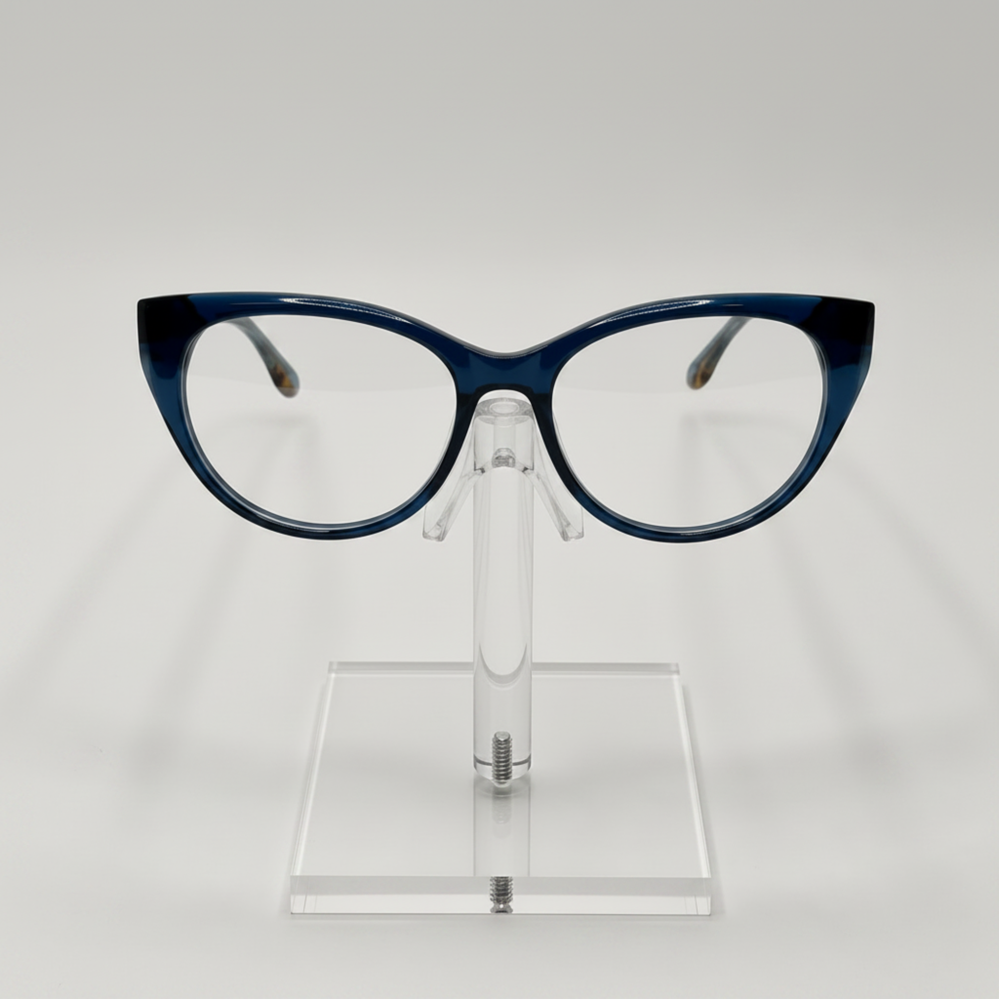 Crazy cat-eye eyeglasses with a dark blue acetate frame, displayed on a clear acrylic stand against a light gray background.