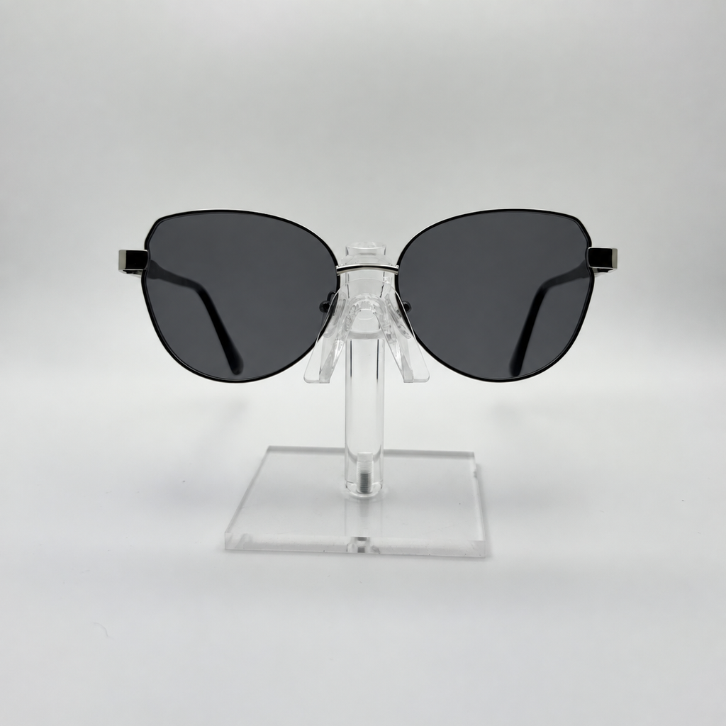 Oversized cat-eye sunglasses with dark gray lenses and a thin black metal frame, displayed on a clear acrylic stand against a light gray background.