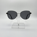 Oversized cat-eye sunglasses with dark gray lenses and a thin black metal frame, displayed on a clear acrylic stand against a light gray background.