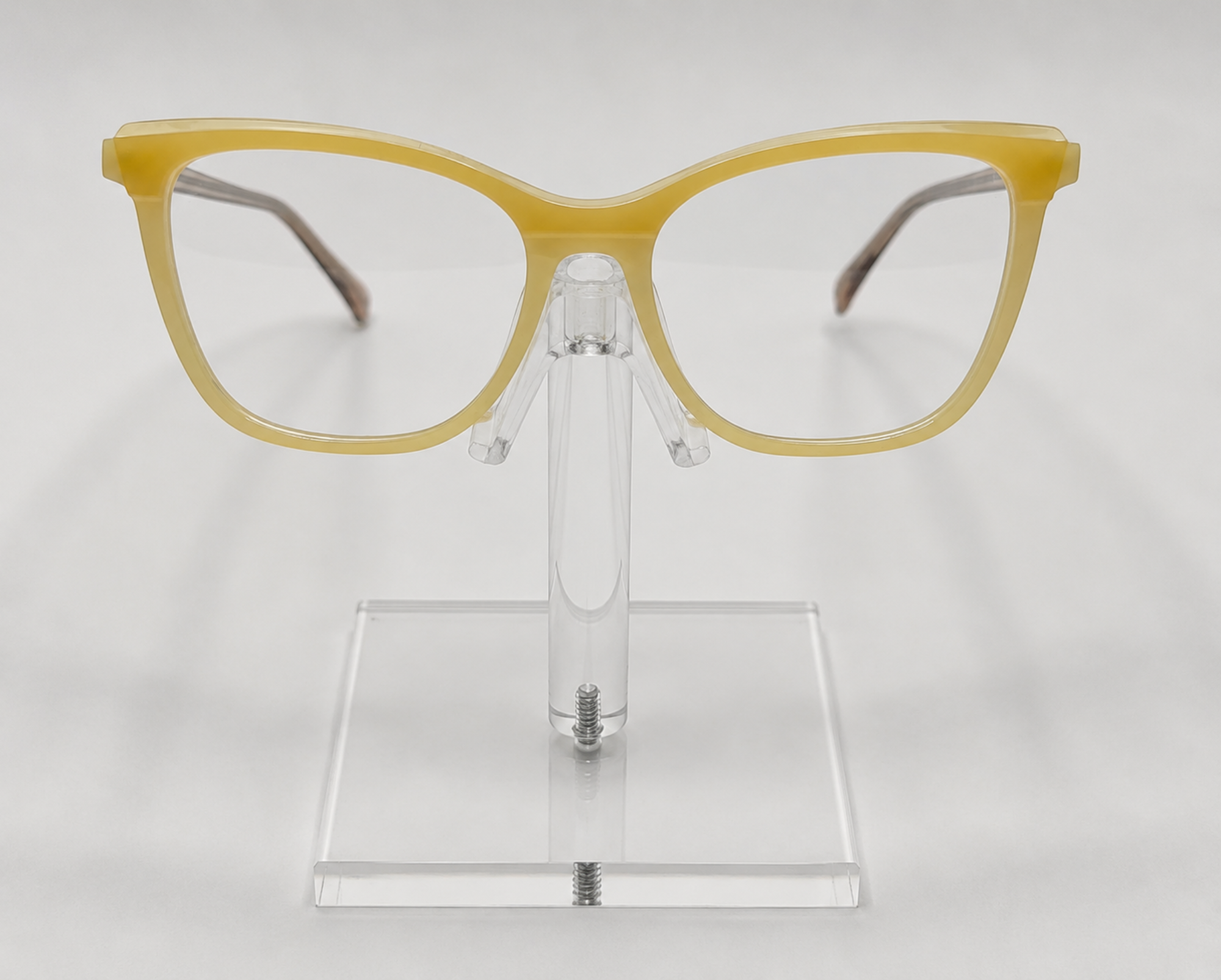Yellow cat-eye eyeglasses displayed on a clear acrylic stand against a light gray background.